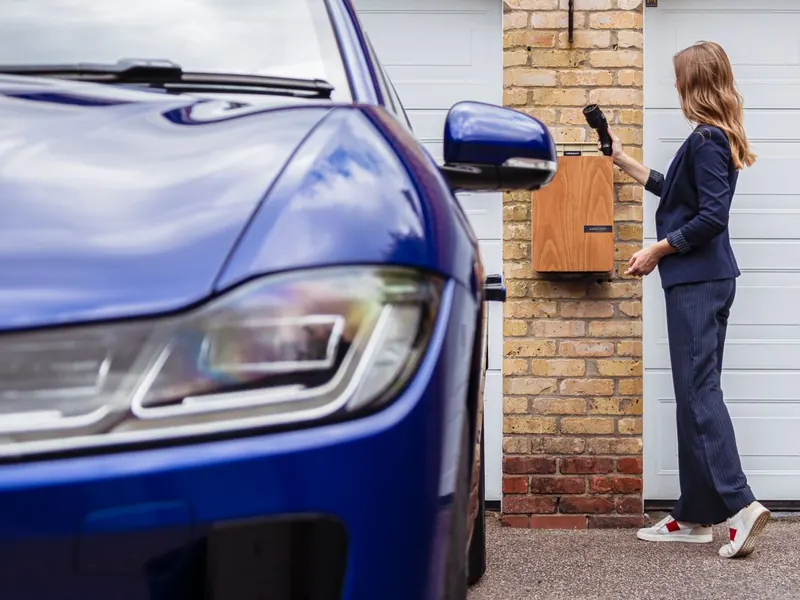 Person lädt ein Elektroauto an einer an der Hauswand montierten Wallbox
